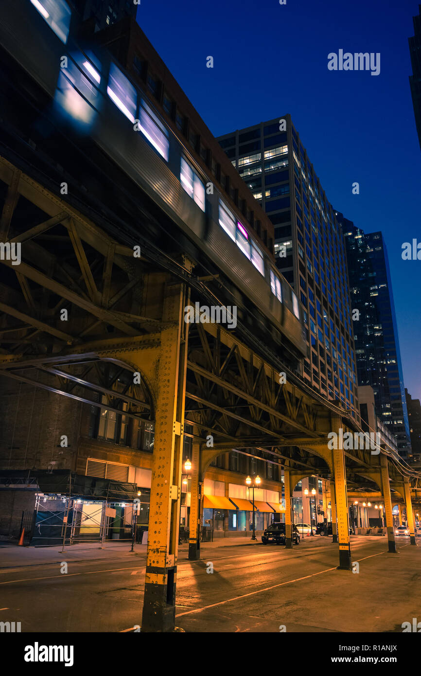 Un CTA metropolitana treno su un vintage Chicago Loop elevato ponte ferroviario di notte con lo skyline e grattacieli in background Foto Stock