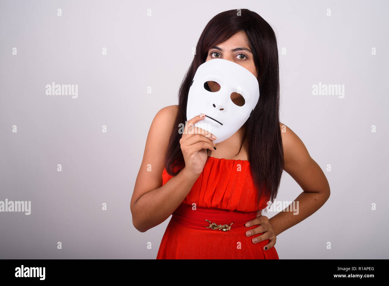 Studio shot della giovane donna persiano che copre il viso con maschera bianca Foto Stock