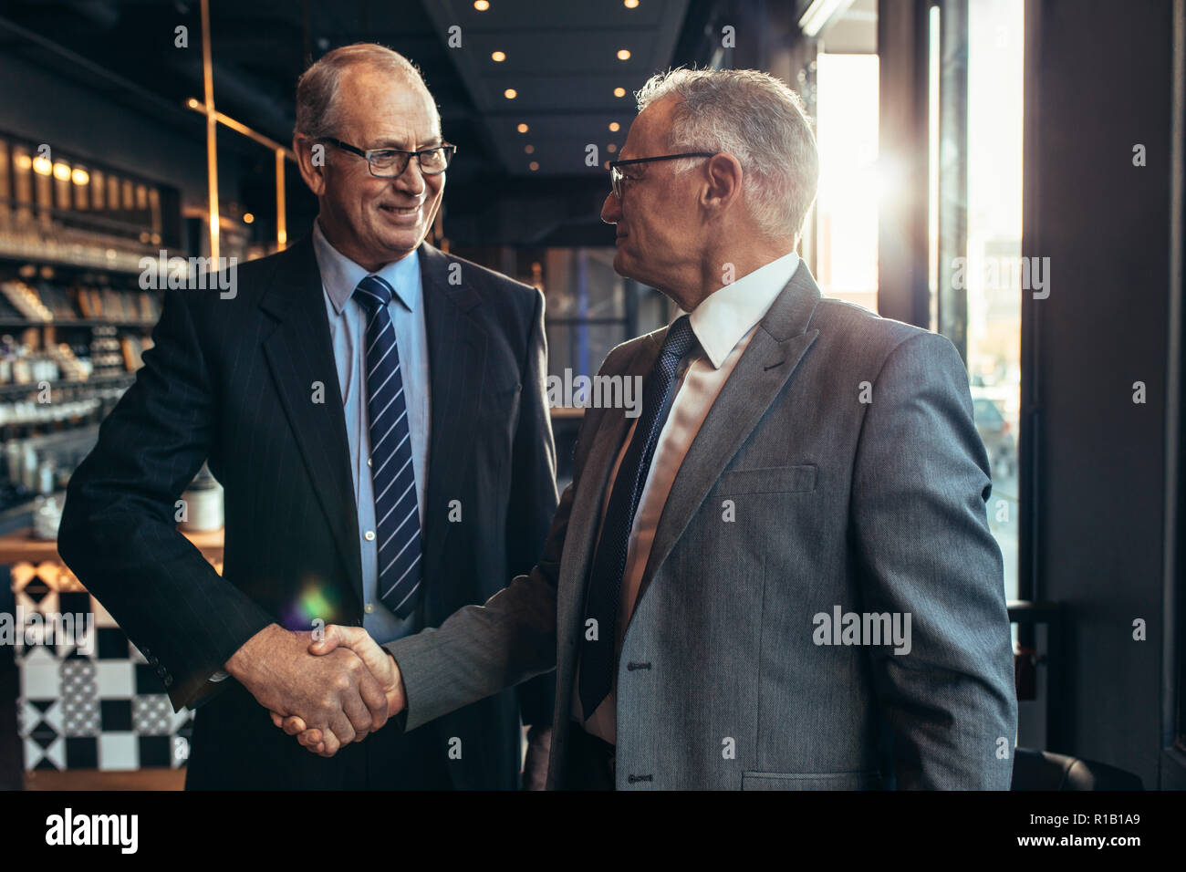 Due uomini d'affari di alto livello si incontrano al bar stringendo la mano. i partner commerciali si scagliano la mano presso la moderna caffetteria. Foto Stock