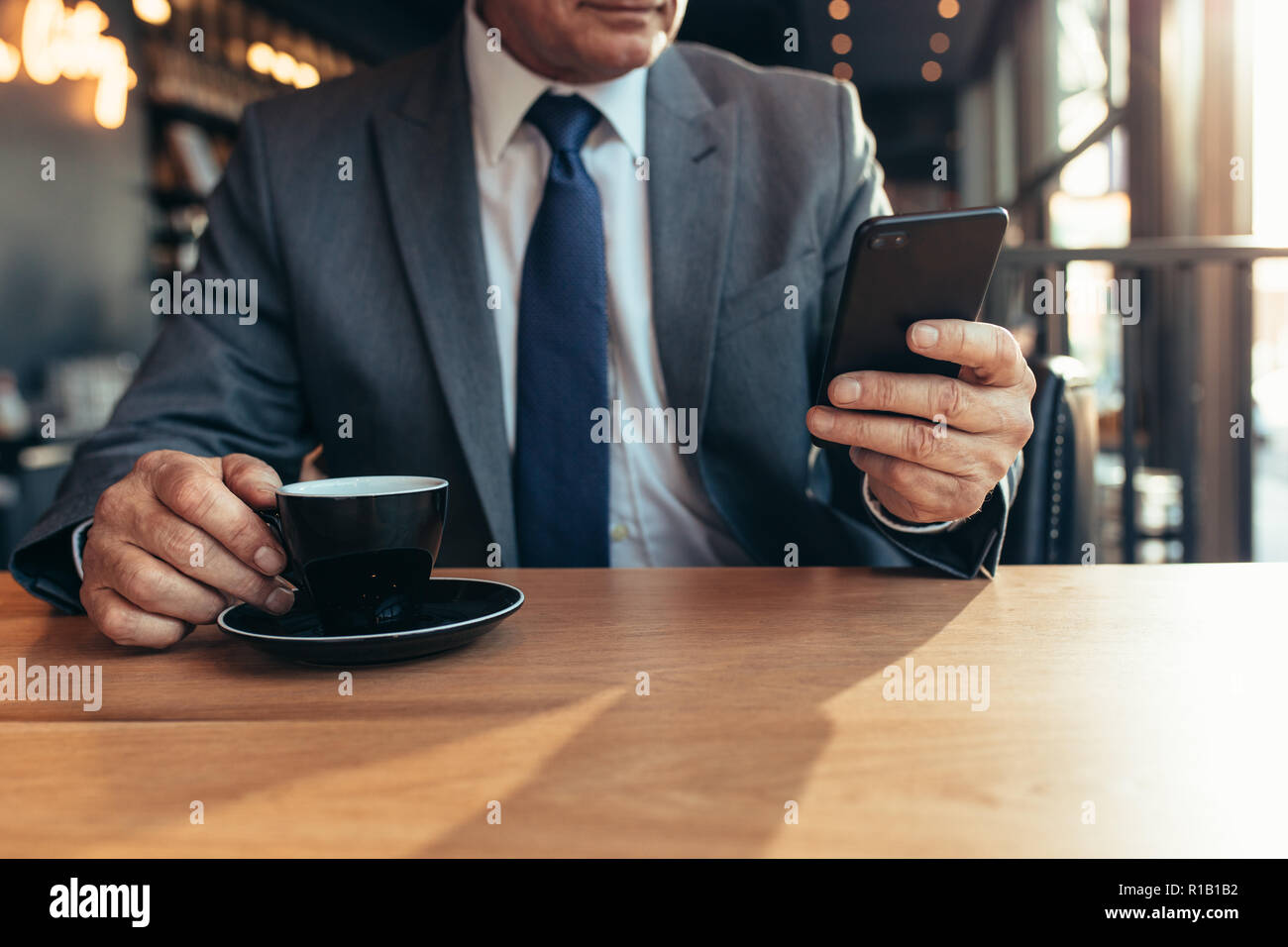 Ritagliato colpo di smart phone in mano a un imprenditore senior con caffè sul tavolo del bar. Imprenditore senior di scrivere messaggi su telefono cellulare presso la caffetteria. Foto Stock