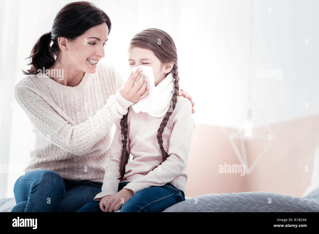 Madre positivo aiutando la figlia con soffia il naso Foto Stock