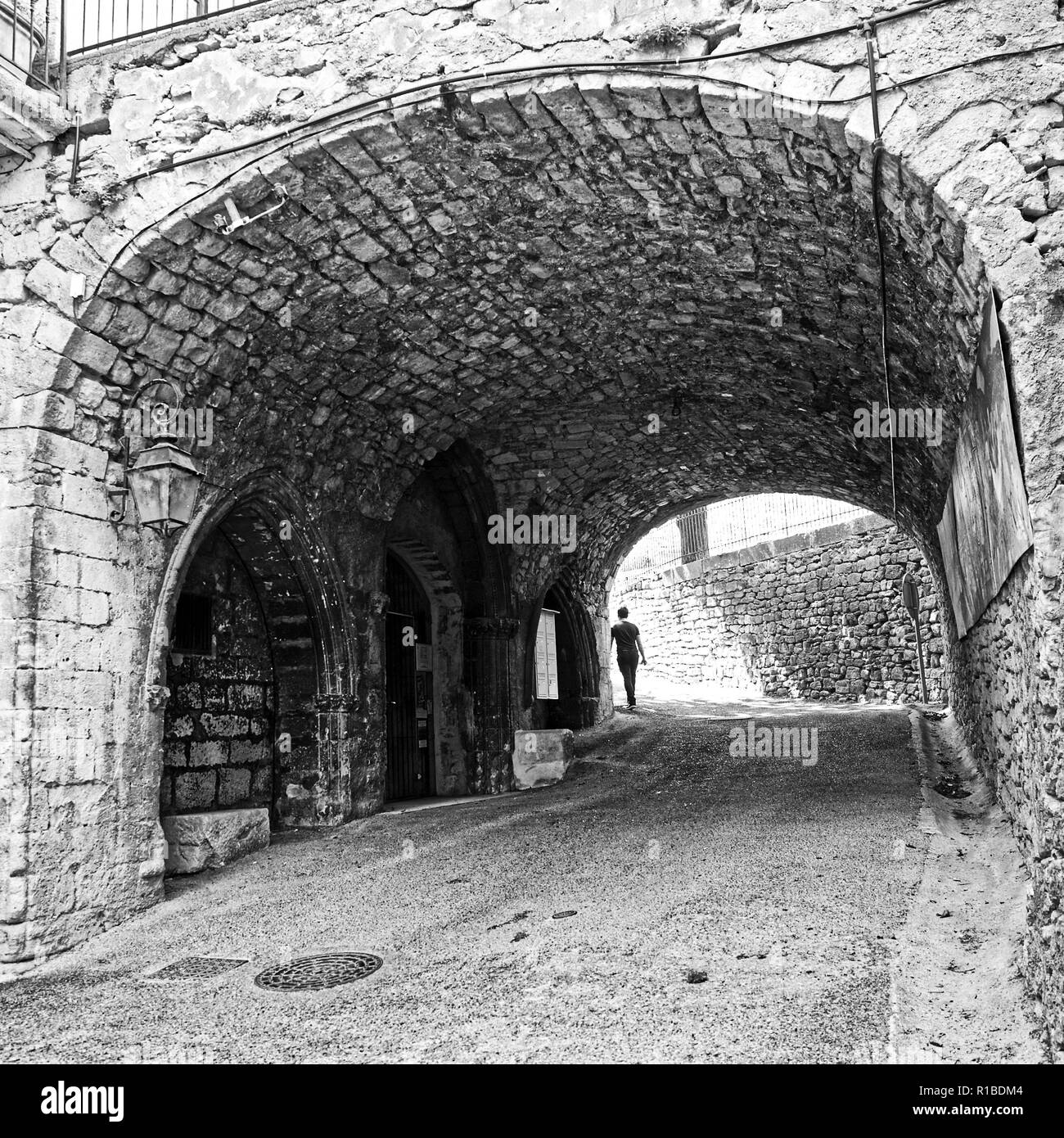 Giovane uomo a piedi dal telespettatore attraverso un antico arco nel sud della Francia Foto Stock