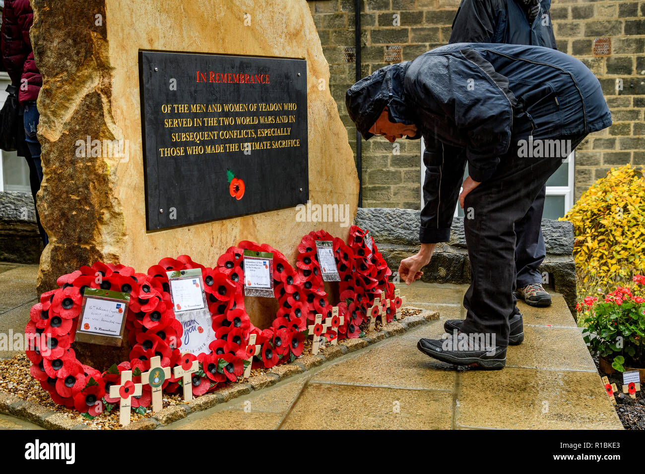 Yeadon, Leeds, West Yorkshire, Regno Unito 11 novembre, 2018. Close-up della placca iscrizione e croci & poppy ghirlande di cui alla base del nuovo memoriale di guerra la pietra di fronte Yeadon Chiesa Metodista, anniversario della fine della Prima Guerra Mondiale. Un uomo si piega verso il basso posizionando una croce in terra. Ian Lamond/Alamy Live News. Foto Stock