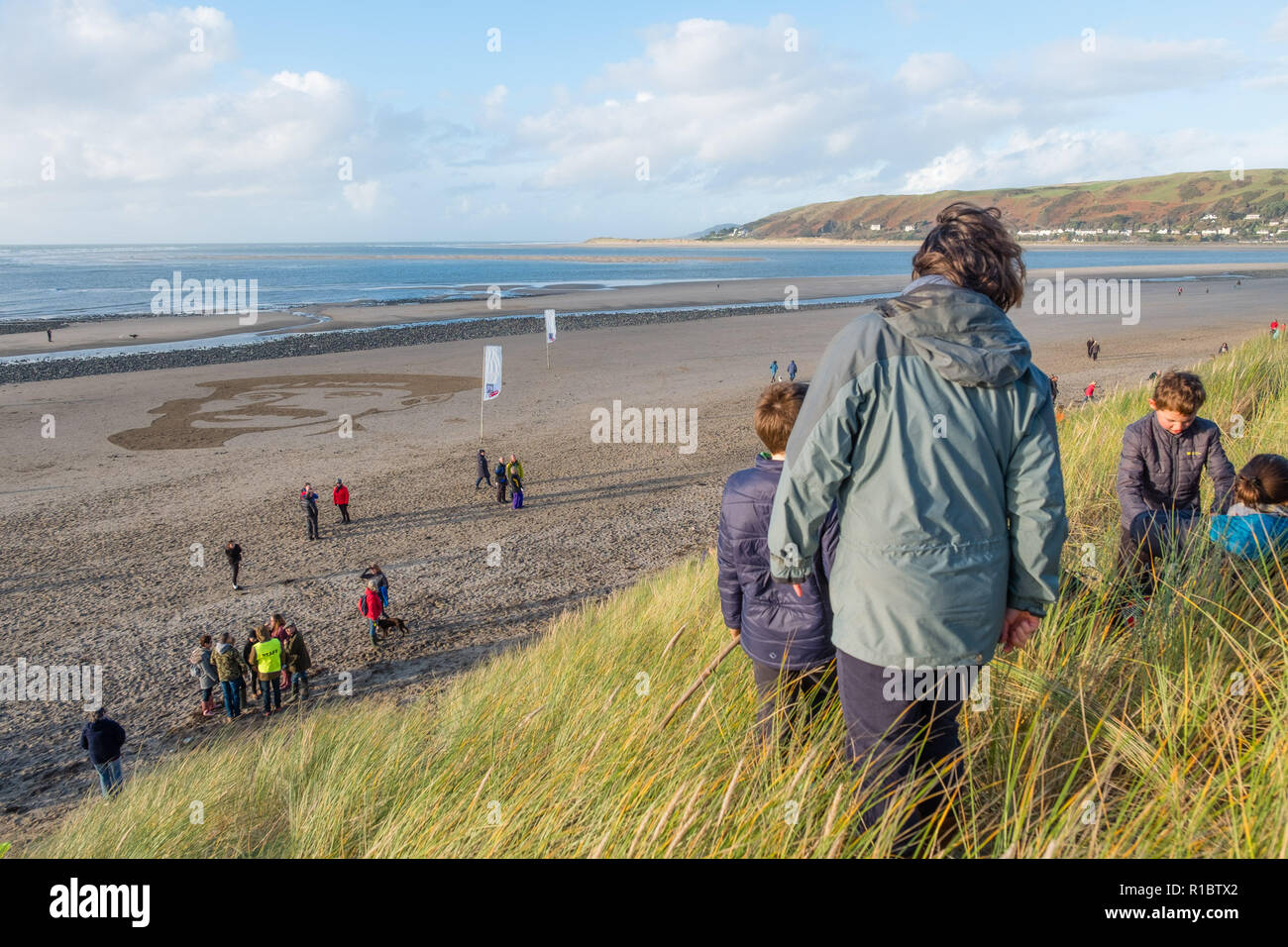 Ynyslas Wales UK, 11/11/2018. La gente guarda come un gigante 30mx30m sabbia ritratto di RICHARD DAVIES, deck mano, dal vicino villaggio di Borth, che ha servito nella Royal Navy nella prima guerra mondiale, è scolpita nella sabbia sulla spiaggia di Ynyslas , appena a nord di Aberystwyth sulla West Wales coast. Concepito dal regista Danny Boyle, questo effimero perforato del memorial arte - Pagine di mare - è uno dei 28 creato su spiagge in tutto il Regno Unito in questo giorno, ricordo la domenica, il centesimo anniversario dell'armistizio che ha portato a termine la prima guerra mondiale Photo credit Keith Morris / Alamy Live News Foto Stock