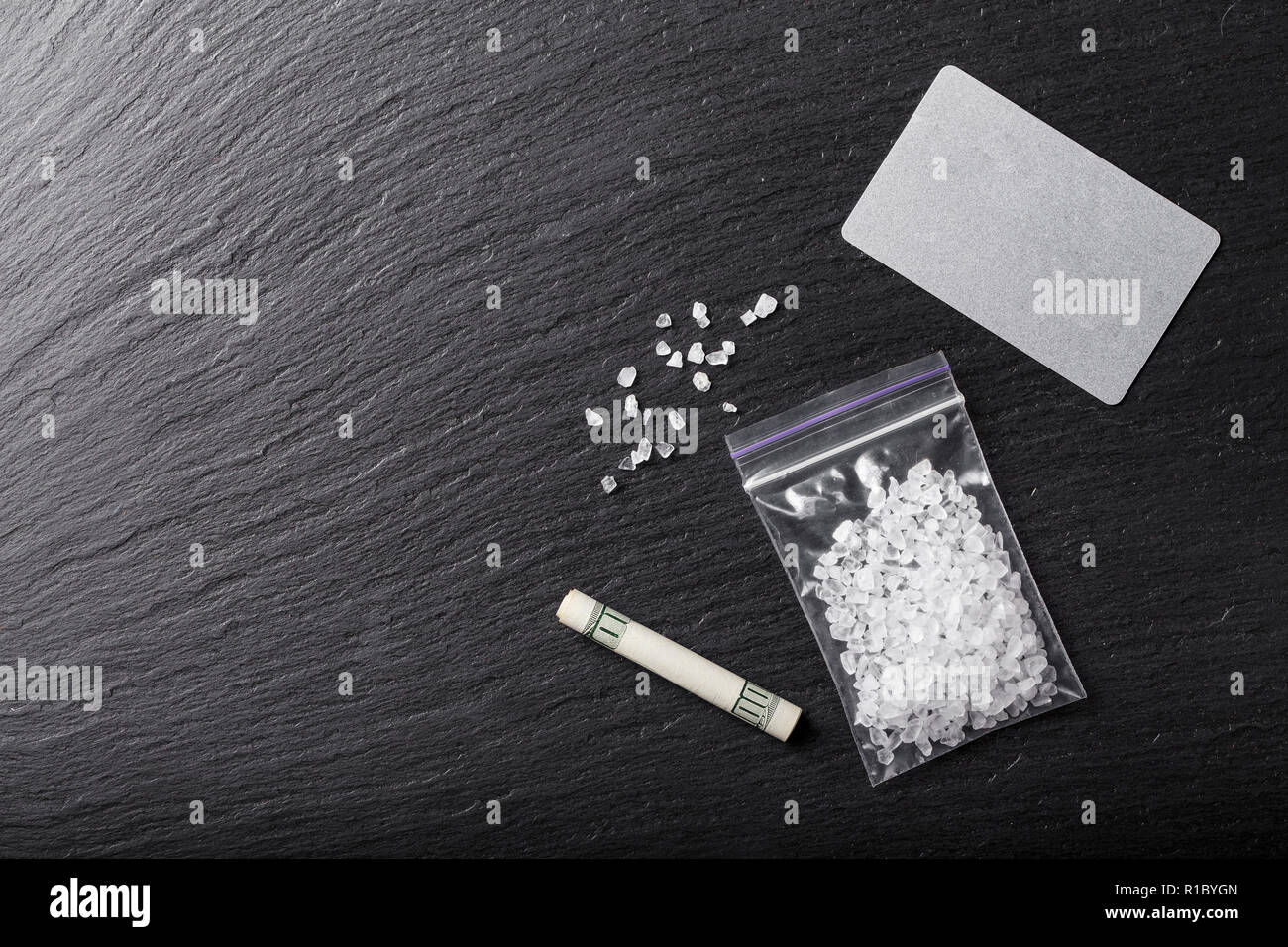 Cristalli bianchi di farmaci in una borsa su una tavola nera. accanto ad esso è una $ 100 bill ripiegato a tubo Foto Stock
