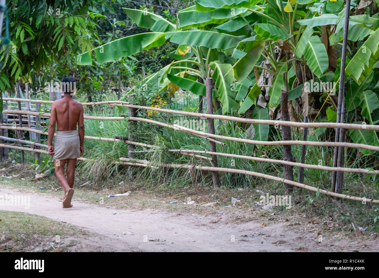 Don Det, Laos - Aprile 23, 2018: a piedi nudi uomo locale a piedi attraverso un sentiero di Don Det villaggio vicino al confine con la Cambogia Foto Stock