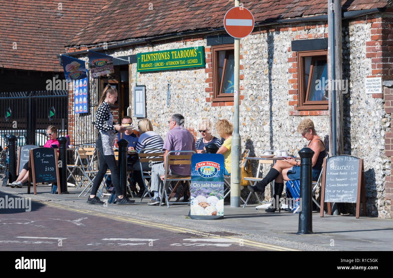 Una giovane cameriera che porta cibo ai clienti seduti fuori al Flintstones Tearooms Cafe di Emsworth, Hampshire, Inghilterra, Regno Unito. Foto Stock