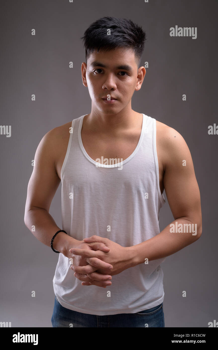 Bel giovane uomo asiatico indossando tank top contro backgroun grigio Foto Stock