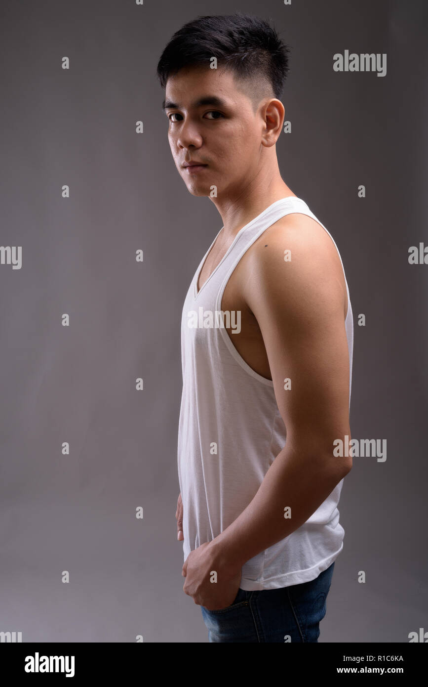 Bel giovane uomo asiatico indossando tank top contro backgroun grigio Foto Stock