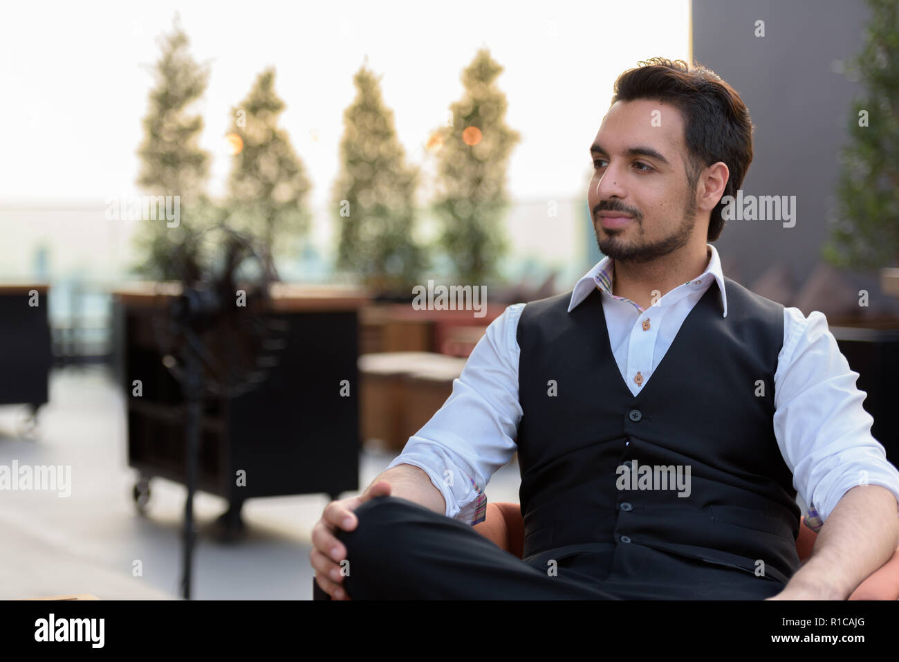 Bel giovane uomo indiano pensare mentre è seduto a riposo sul tetto Foto Stock