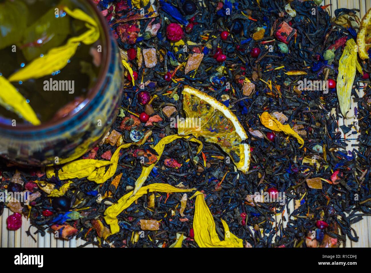 Fragranti tè verde giallo con petali di fiori è prodotta in una tazza con la cultura cinese ornamenti. Una tazza si erge contro una diffusa tè essiccato Foto Stock