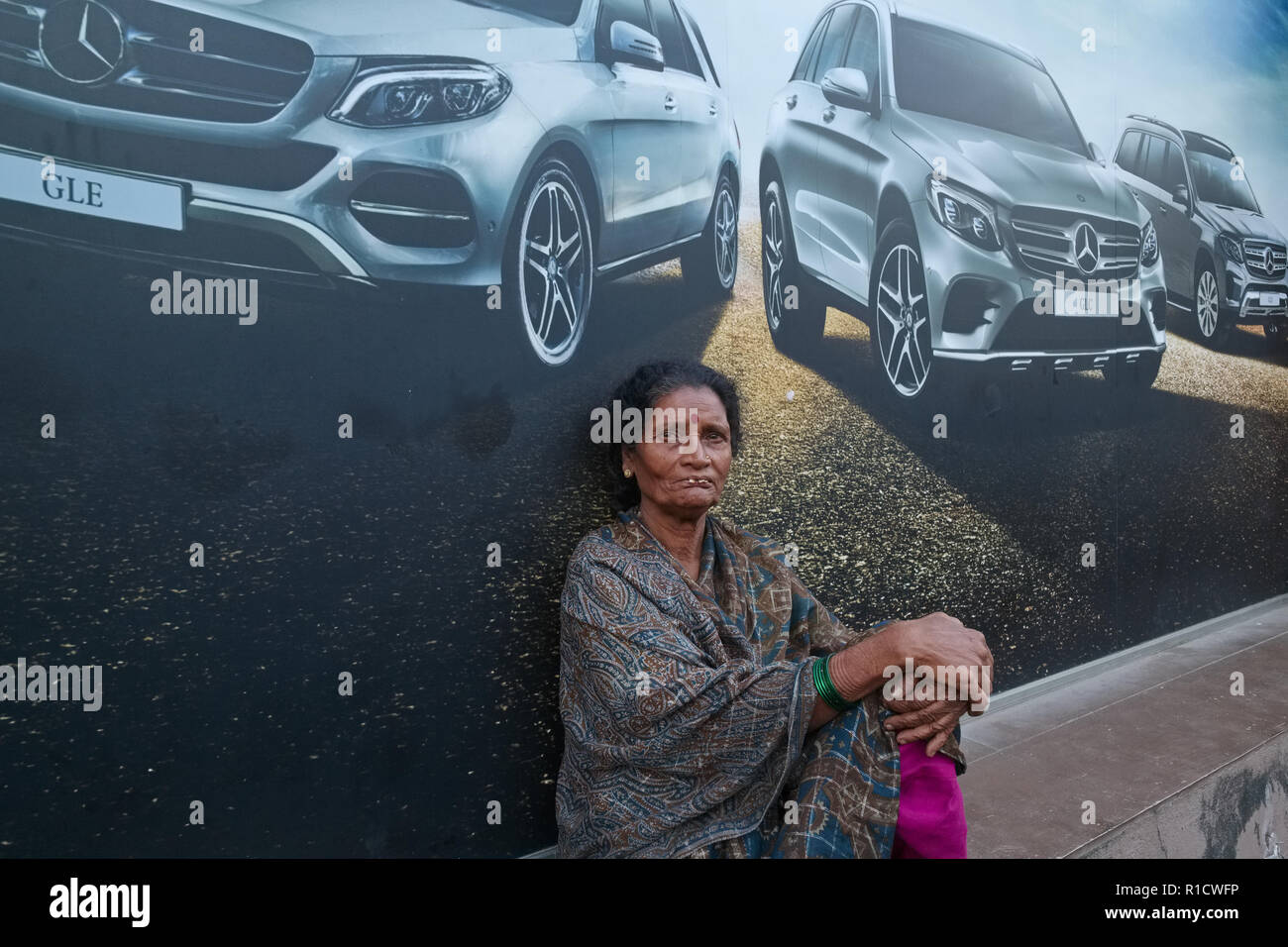 Una donna dalla parte inferiore gli strati sociali in Mumbai, India, seduta al di sotto di un annuncio per le vetture Mercedes Foto Stock