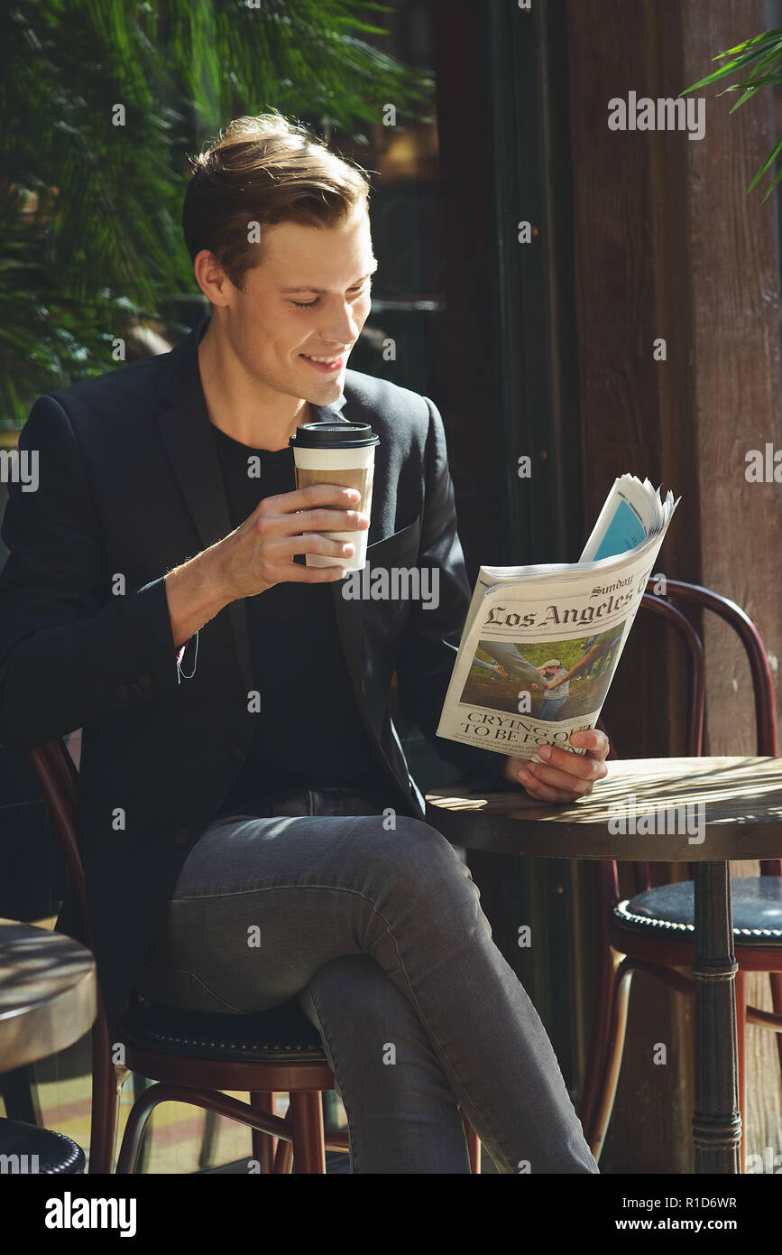 Un imprenditore ritratto, si siede in un bar con una tazza di caffè leggendo un giornale. Il successo di un giovane imprenditore ritratto. Foto Stock