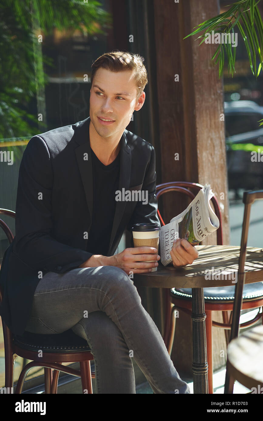 Un imprenditore ritratto, si siede in un bar con una tazza di caffè tenendo un giornale. Il successo di un giovane imprenditore ritratto. Foto Stock