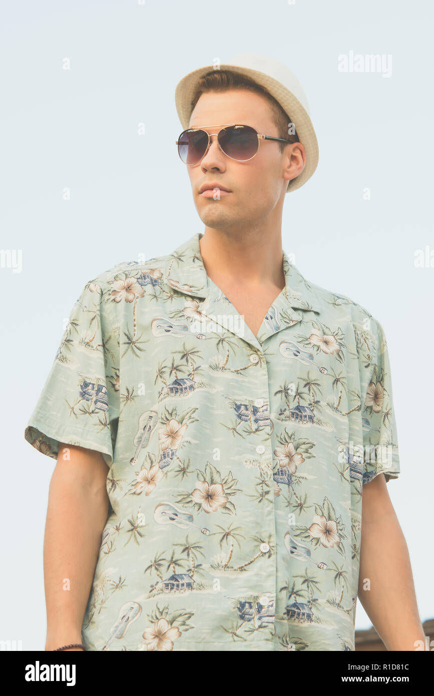 Un bel modello maschile che pongono in estate shirt outdoor contro un cielo blu. Egli indossa una veste bianca cappello Fedora e aviator occhiali da sole. Foto Stock