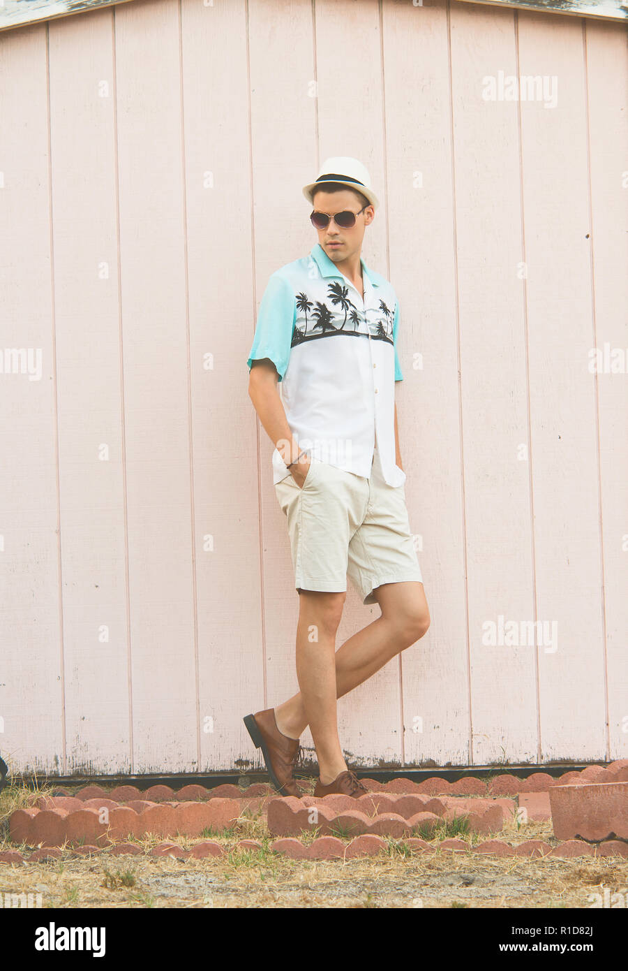 Un bel modello maschile in posa di vestiti estivi all'aperto in piedi contro una normale parete in legno. Foto Stock