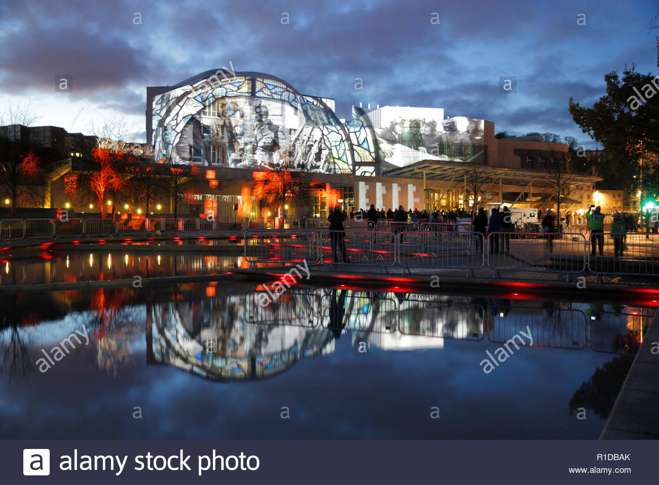 Edinburgh, Regno Unito. 11 Novembre, 2018. L'edificio del parlamento scozzese illuminata sul il giorno dell'Armistizio con immagini che raccontano la storia della guerra mondiale 1 conflitto a fianco di un rotolo di onore di coloro che sono morti, riflesso nel laghetto ornamentale. Credito: Craig Brown/Alamy Live News. Foto Stock