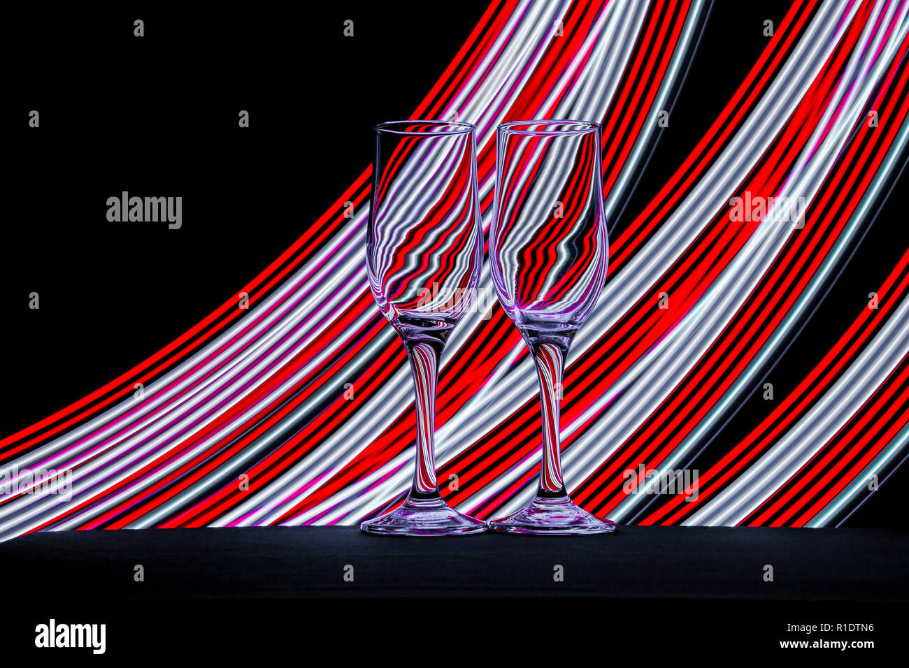 Due bicchieri di champagne con strisce multicolore di luci al neon dietro  di loro creato con una torcia a LED Foto stock - Alamy