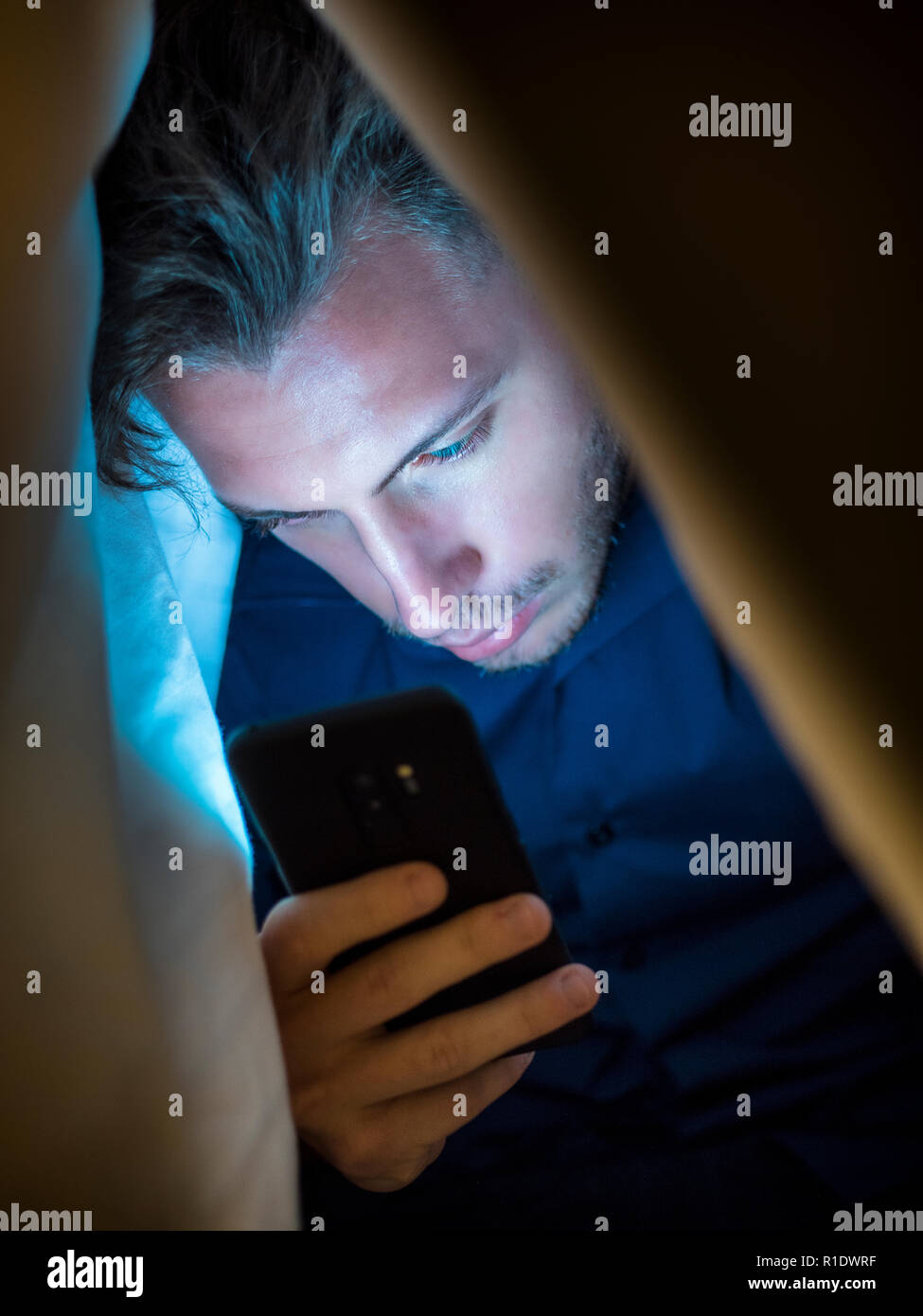 Giovane uomo nascondendosi sotto una coperta mentre si utilizza un telefono  cellulare per la navigazione in internet o per chattare privatamente online  Foto stock - Alamy