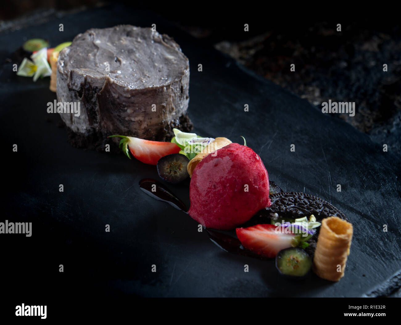 Oreo Cheesecake al buio su un sfondo di ardesia con sorbetto di fragole Foto Stock