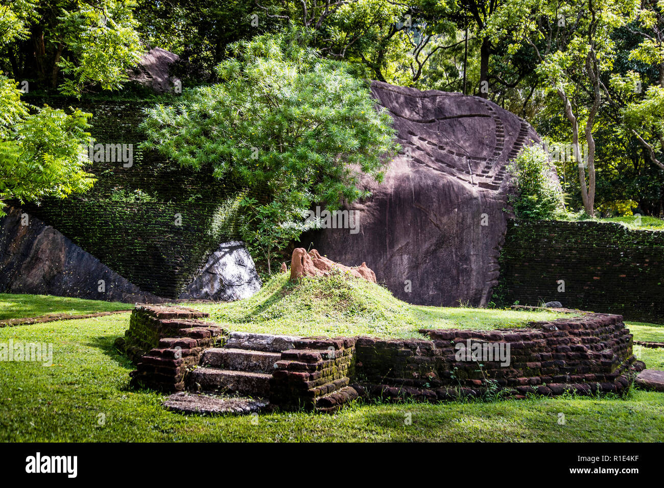 Le pareti in mattoni si accoccolano delicatamente contro le rocce naturali sotto la fortezza rocciosa di Sigiriya, Sri Lanka Foto Stock