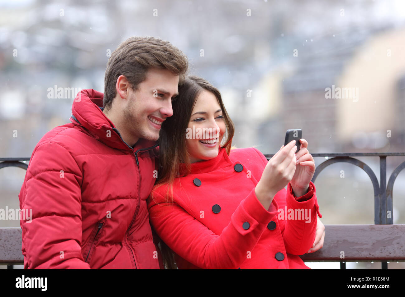 Coppia felice in rosso il controllo smart phone contenuto su vacanze inverno Foto Stock