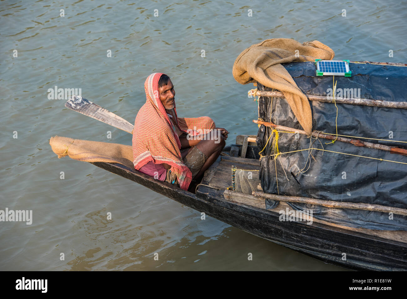 La giustapposizione di tradizione e modernità: un pescatore in carica della sua umile barca a remi si basa su pannelli solari per caricare i suoi gadget! Foto Stock