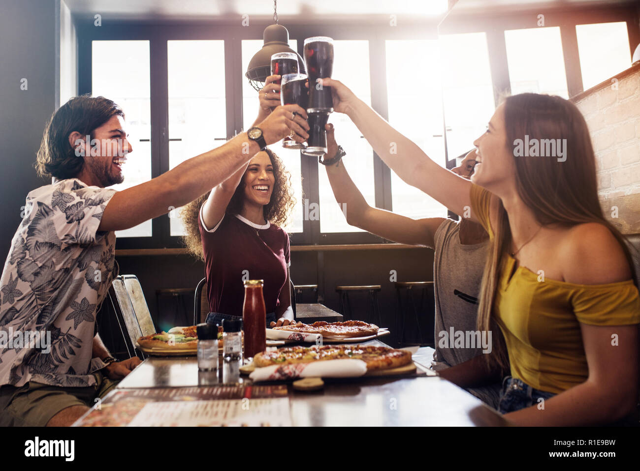 Gruppo di amici fare un brindisi con soft drink bicchieri al ristorante. I giovani seduti ad un tavolo con cibi e bevande di tostatura e di godere di un pasto Foto Stock