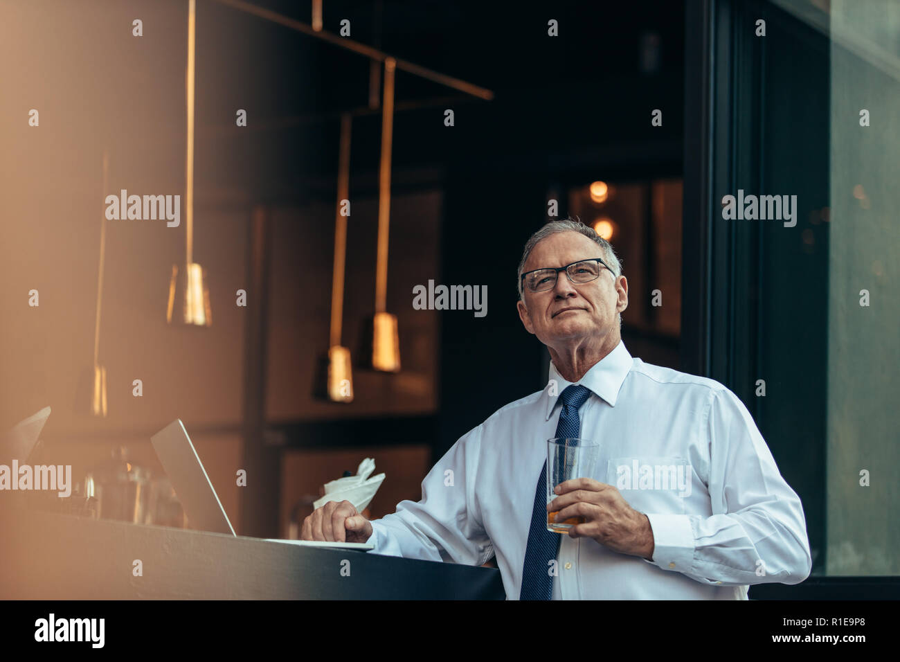 Riflessivo uomo senior con un bicchiere di birra in mano seduto presso il cafe contatore guardando lontano. Maschio maturo imprenditore che guarda lontano pensando pur avendo un b Foto Stock