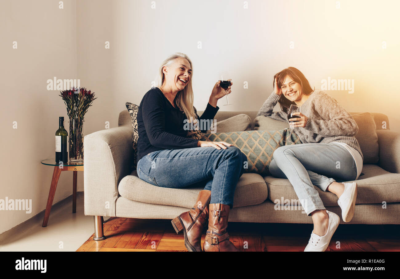 Due felici donne gustando un bicchiere di vino seduti su un lettino a casa. Foto Stock