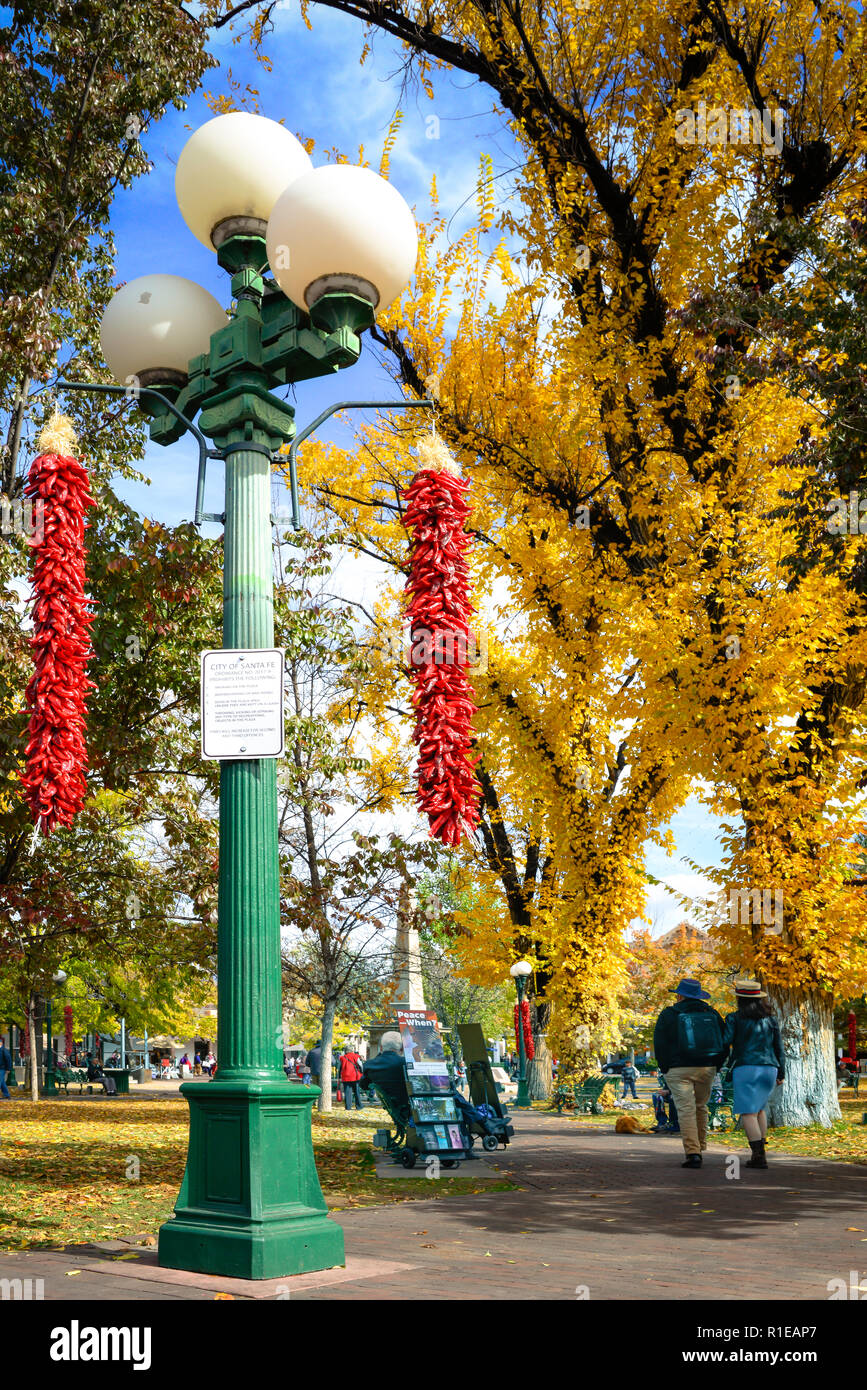 Durante il fogliame di autunno cambia, e il peperoncino rosso ristras appesi da un lampione, persone passeggiare e godersi la Plaza nel centro della città di Santa Fe, NM Foto Stock