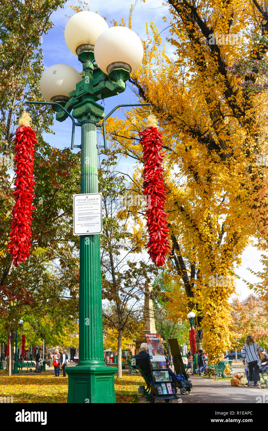 Durante il fogliame di autunno cambia, e il peperoncino rosso ristras appeso dalla lampada posy, persone passeggiare e godersi la Plaza nel centro della città di Santa Fe, NM Foto Stock