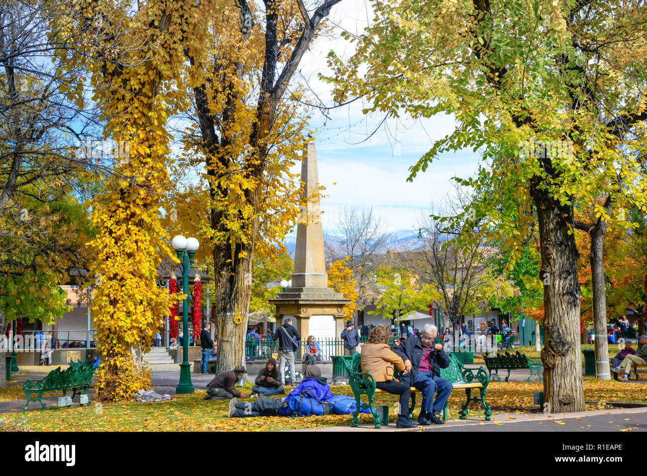 Durante il fogliame di autunno cambia, e il peperoncino rosso ristras appeso dalla lampada posy, persone passeggiare e godersi la Plaza nel centro della città di Santa Fe, NM Foto Stock