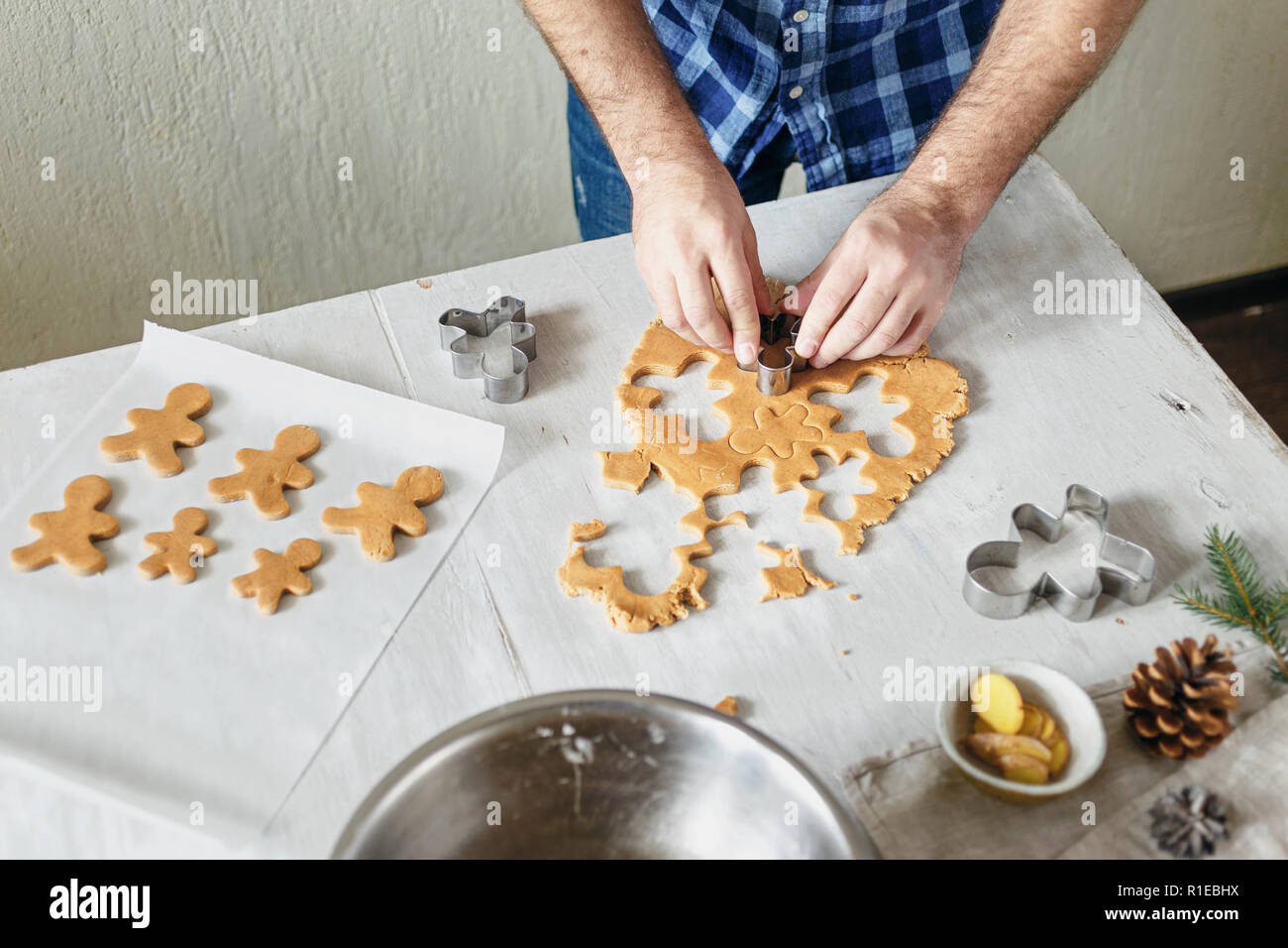 Gastronomia natalizia concetto. L'uomo la cottura gingerbread man cookies nel Natale tavolo in legno nella cucina domestica. Dolce di Natale Foto Stock