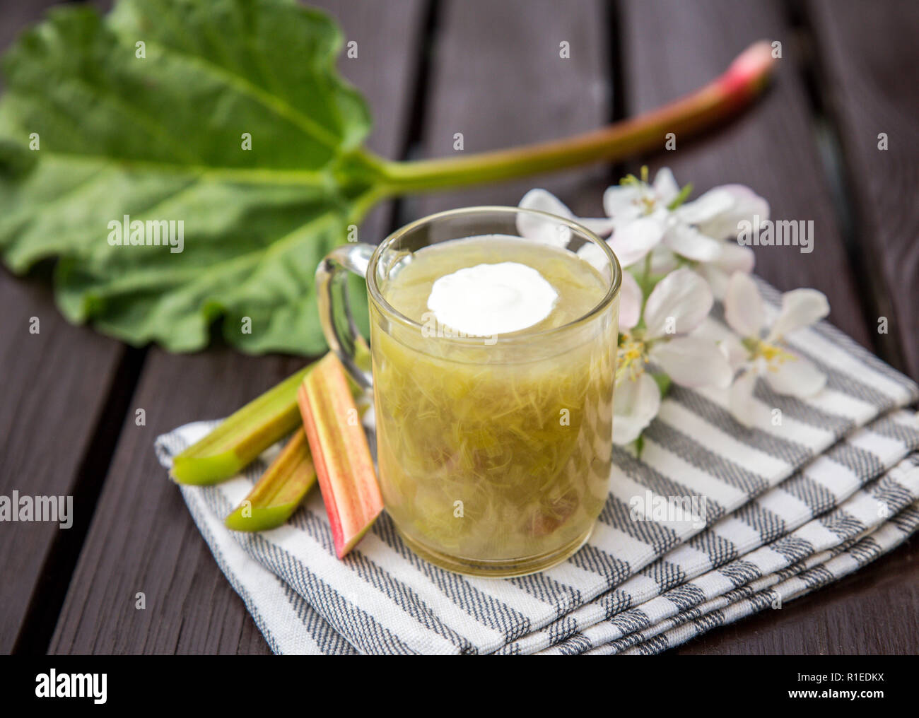 Dolce e aspro kissel o kissel dolce fatto di un rabarbaro (Rheum rhabarbarum) con la spash di panna montata in una coppa trasparente su un sfondo di legno. T Foto Stock