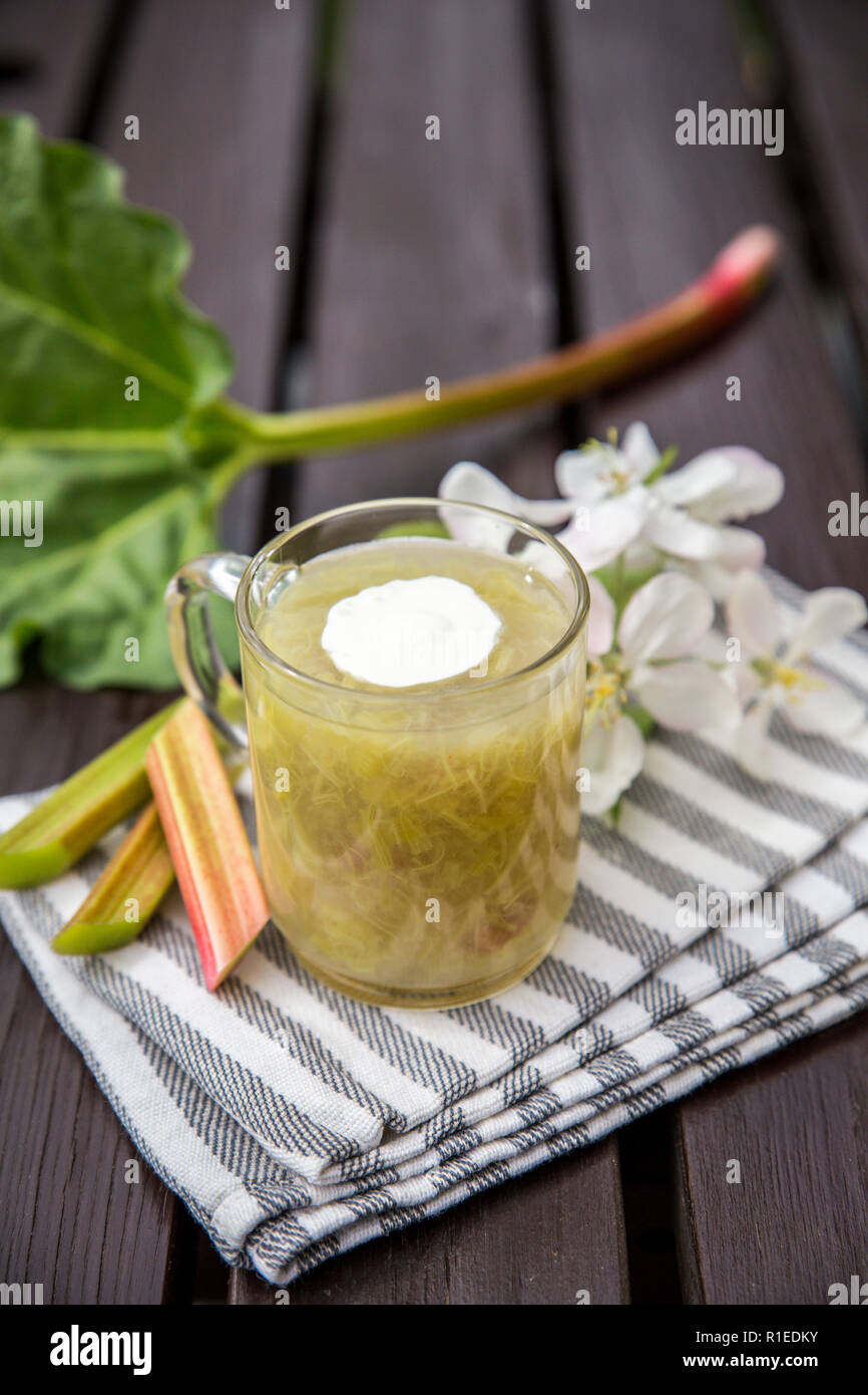 Dolce e aspro kissel o kissel dolce fatto di un rabarbaro (Rheum rhabarbarum) con la spash di panna montata in una coppa trasparente su un sfondo di legno. T Foto Stock