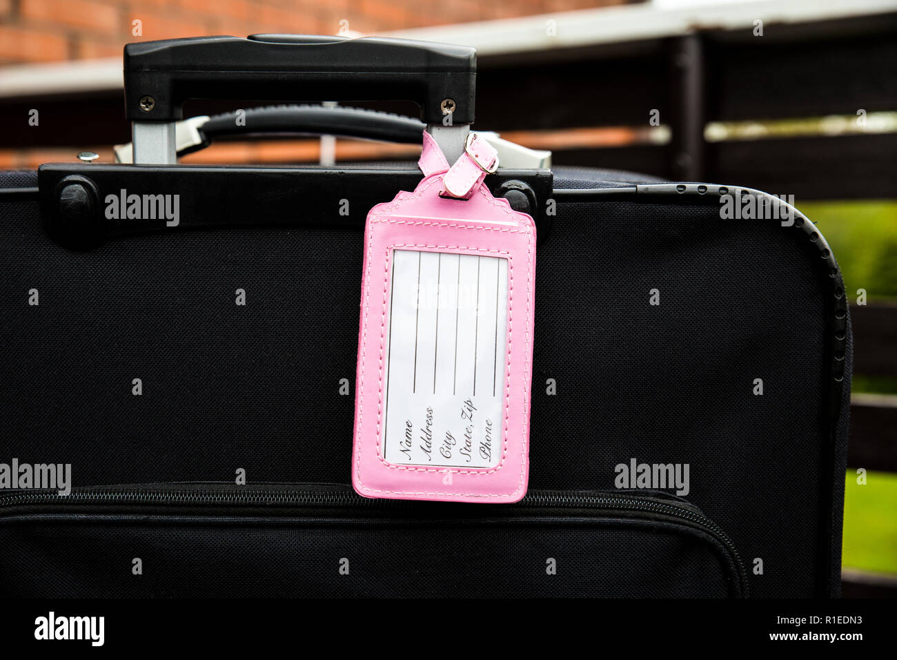 Femminile rosa bagagli vuoti targhetta fissata al bagaglio nero valigia, compilare il tag, nome, indirizzo e telefono di testo. Perso, trovato elemento di design concept. Foto Stock