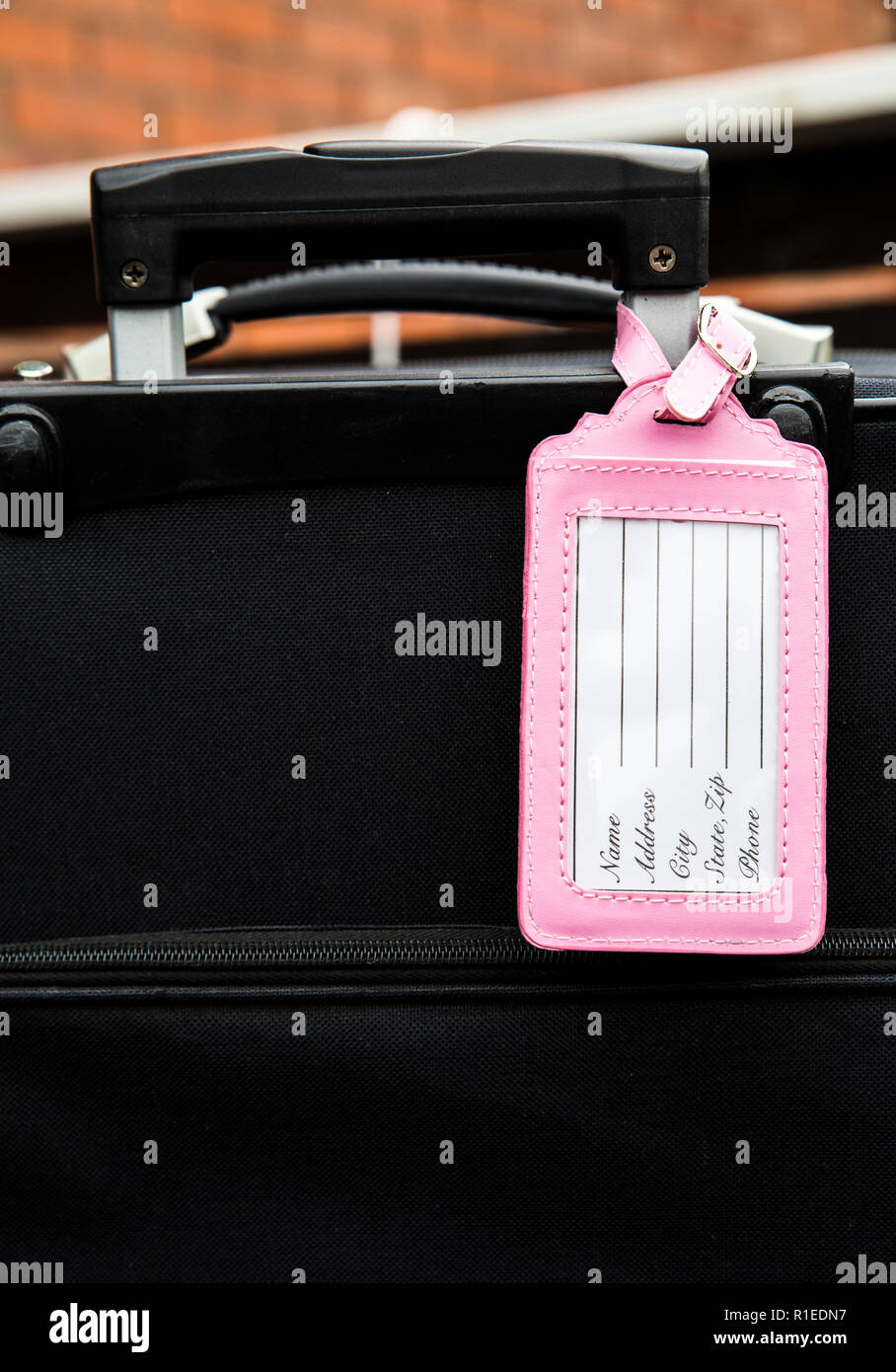 Femminile rosa bagagli vuoti targhetta fissata al bagaglio nero valigia, compilare il tag, nome, indirizzo e telefono di testo. Perso, trovato elemento di design concept. Foto Stock