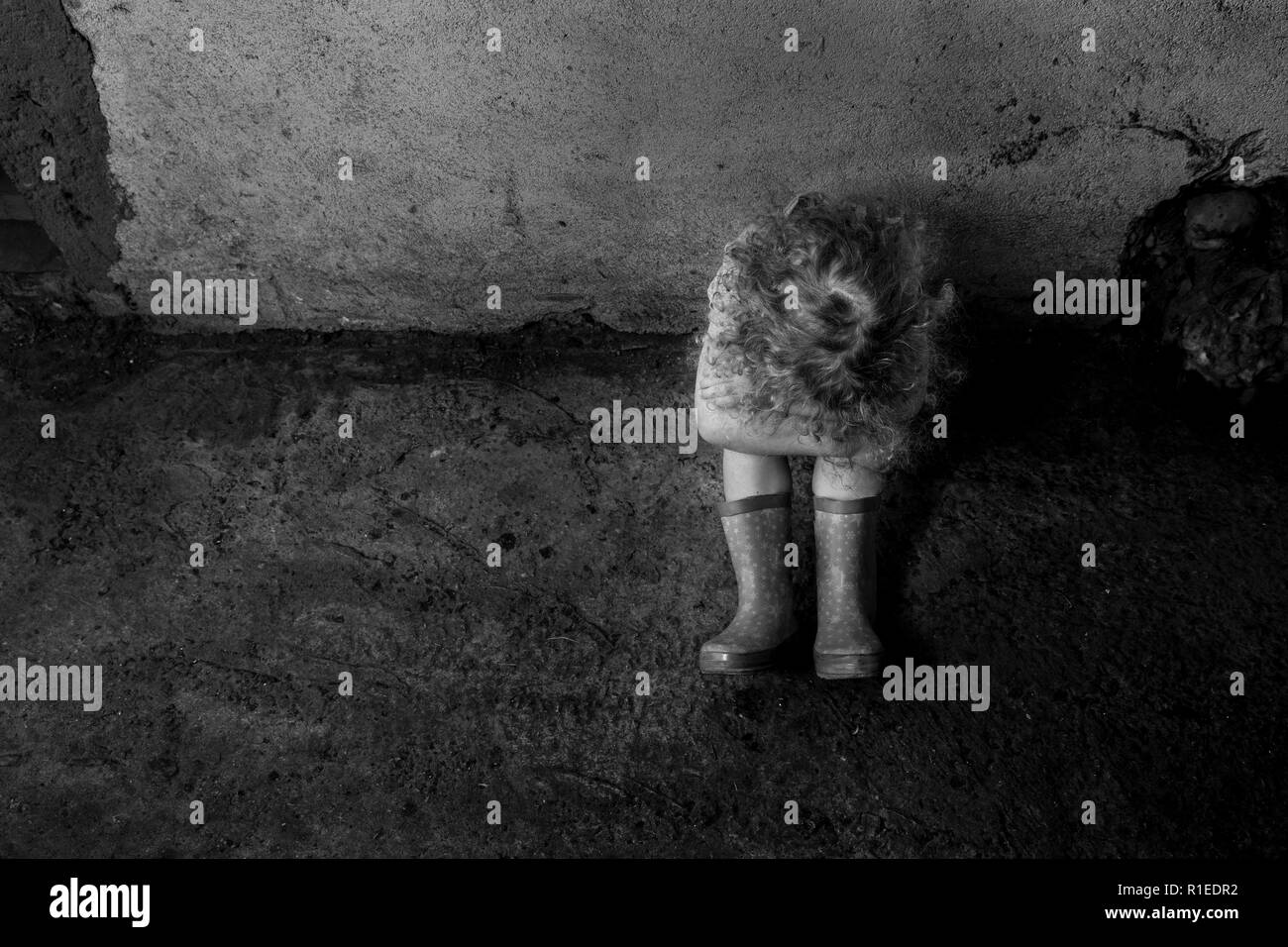 La violenza domestica concetto. Immagine in bianco e nero di paura ragazza bambino seduto da solo nel seminterrato sporco nel buio. Foto Stock