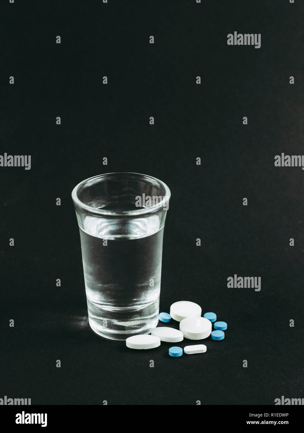 La miscelazione di alcool con farmaci pillole è cattivo concetto pericolose. Un bicchiere di vodka con compresse pillole di farmaci su sfondo nero. Foto Stock