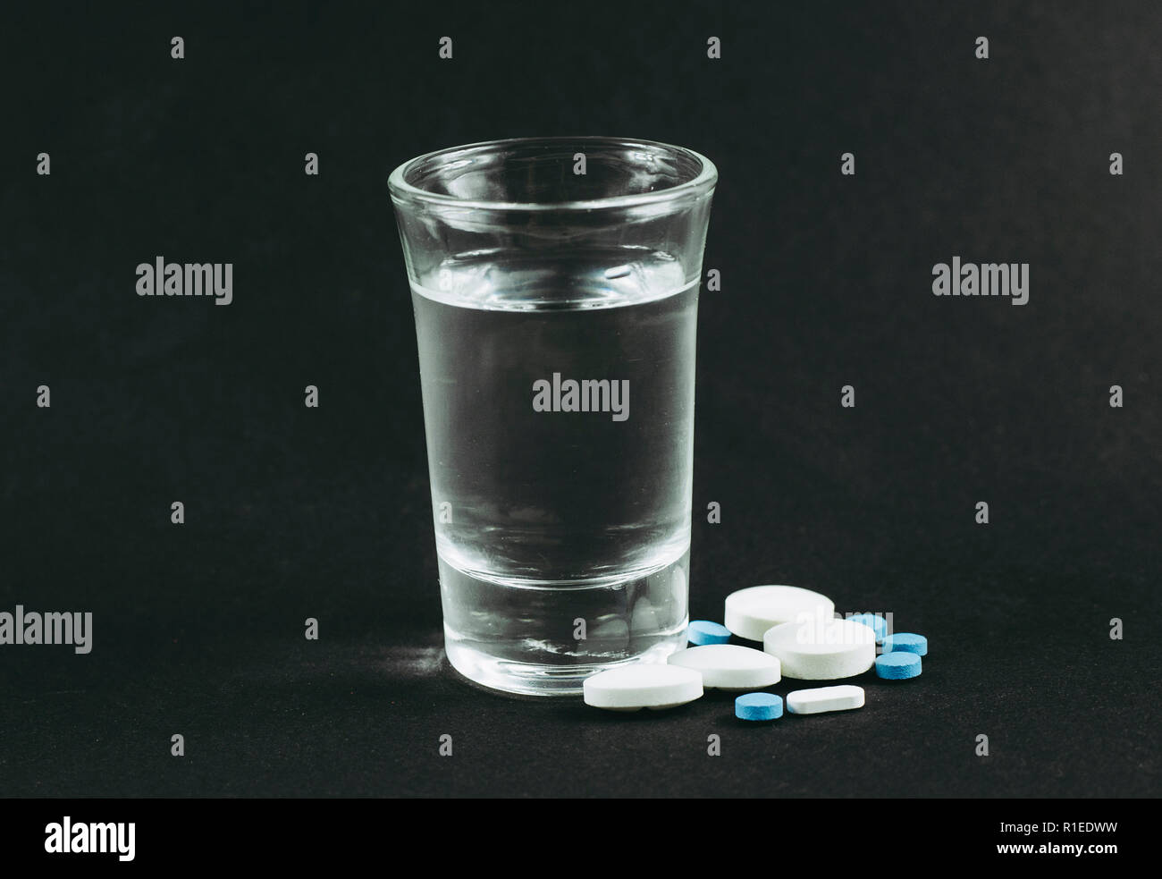 La miscelazione di alcool con farmaci pillole è cattivo concetto pericolose. Un bicchiere di vodka con compresse pillole di farmaci su sfondo nero. Foto Stock