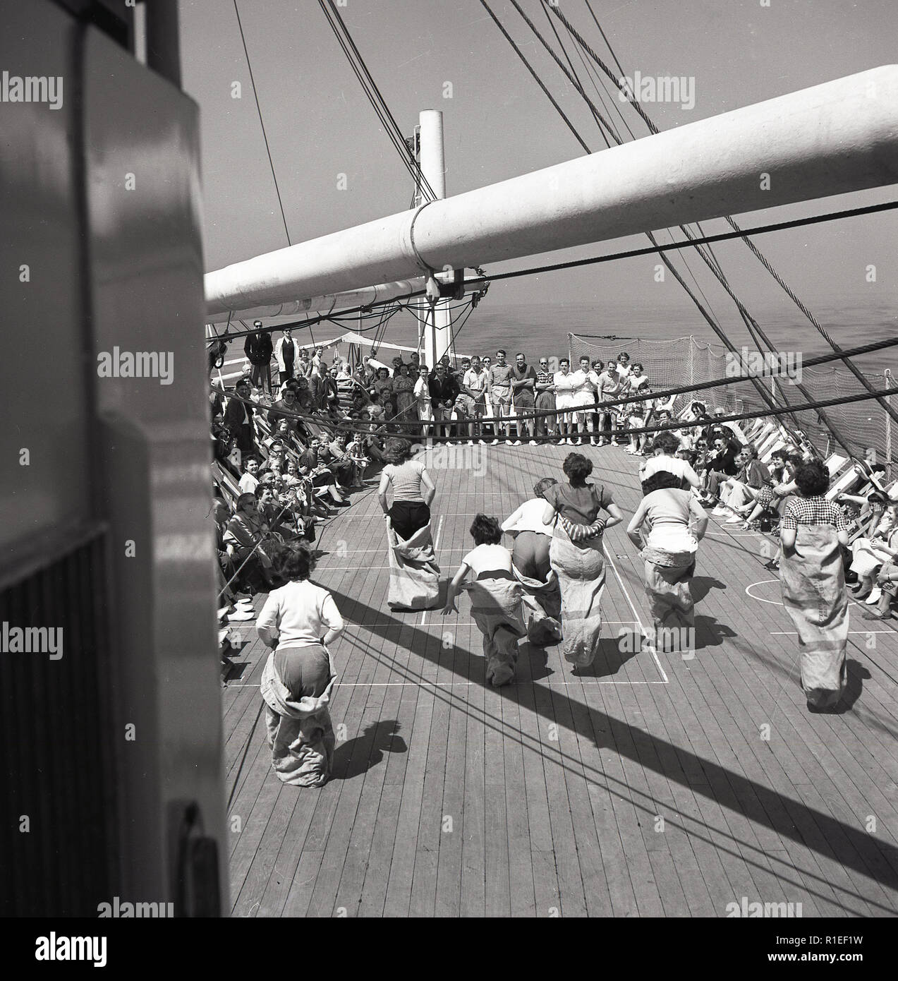 Degli anni Cinquanta, storico in mare a bordo di un' unione-castello steamship, femmina i passeggeri che prendono parte a una sacca gara fuori sul ponte della nave applauditi da guardare gli spettatori, molti seduti in sedie a sdraio. Foto Stock