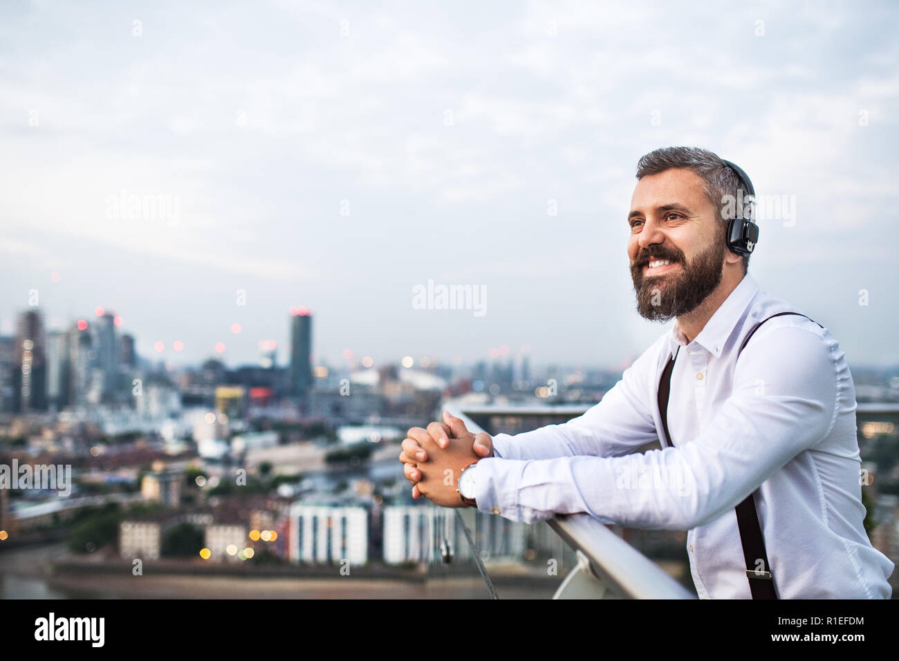 Un imprenditore con le cuffie in piedi contro Londra vista panorama. Copia dello spazio. Foto Stock