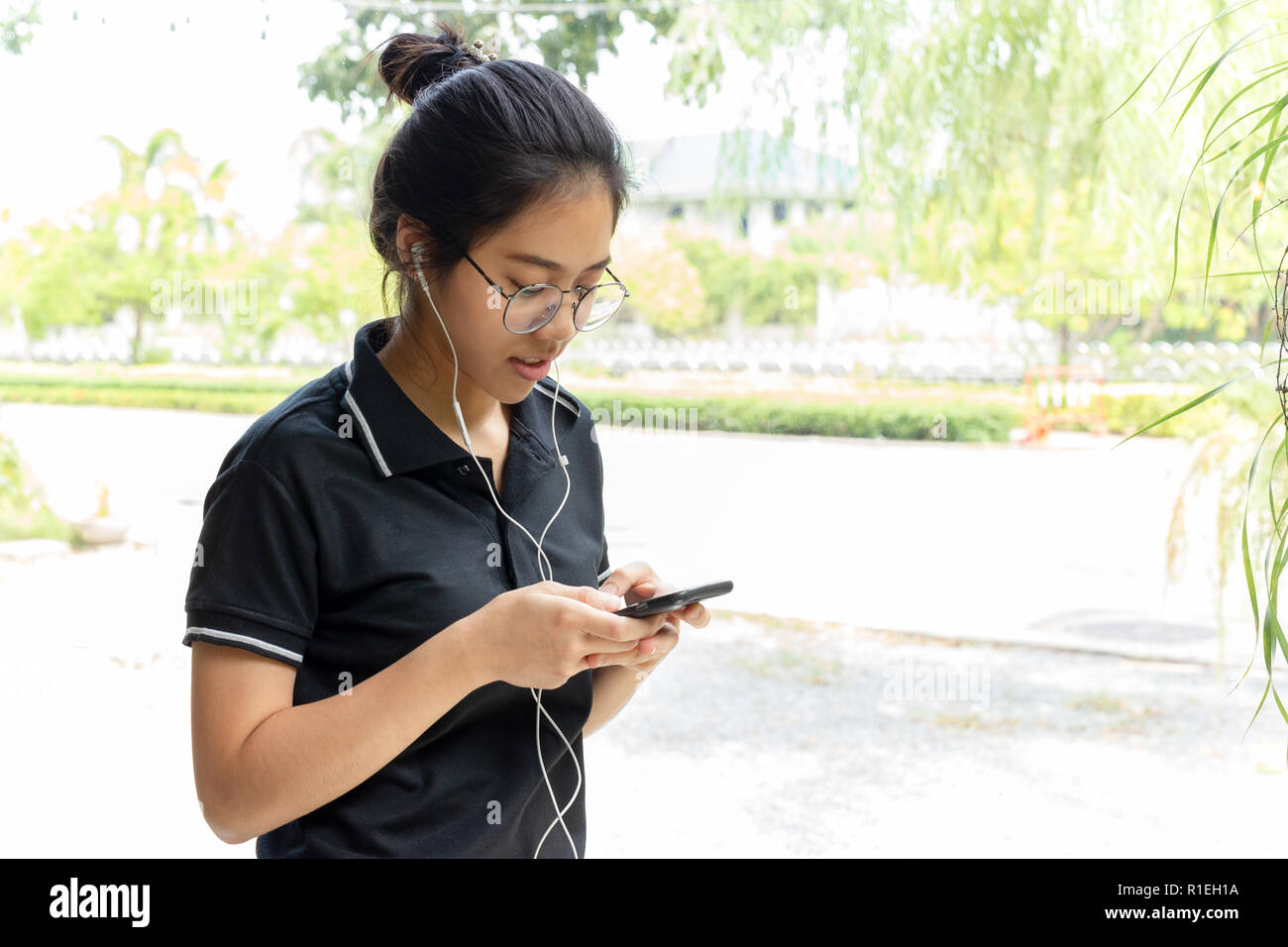 Adolescente asiatica con gli occhiali ascoltando la musica sul telefono cellulare. Foto Stock