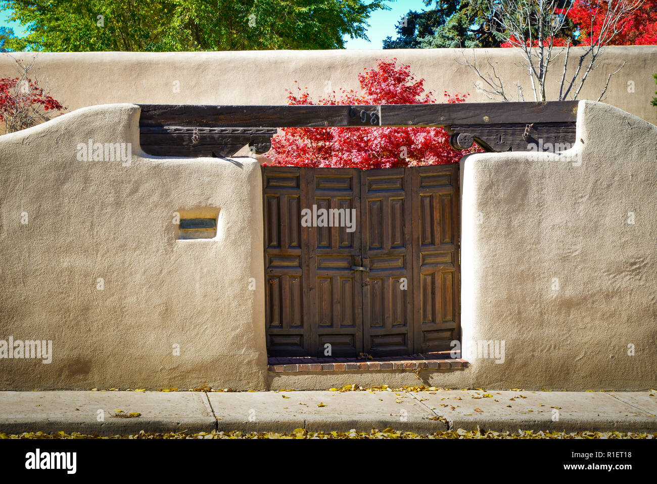 Una suggestiva vista di un muro di adobe e vintage porte in legno con foglie rosse su alberi d'Autunno cortile interno nel quartiere storico di Santa Fe, NM Foto Stock