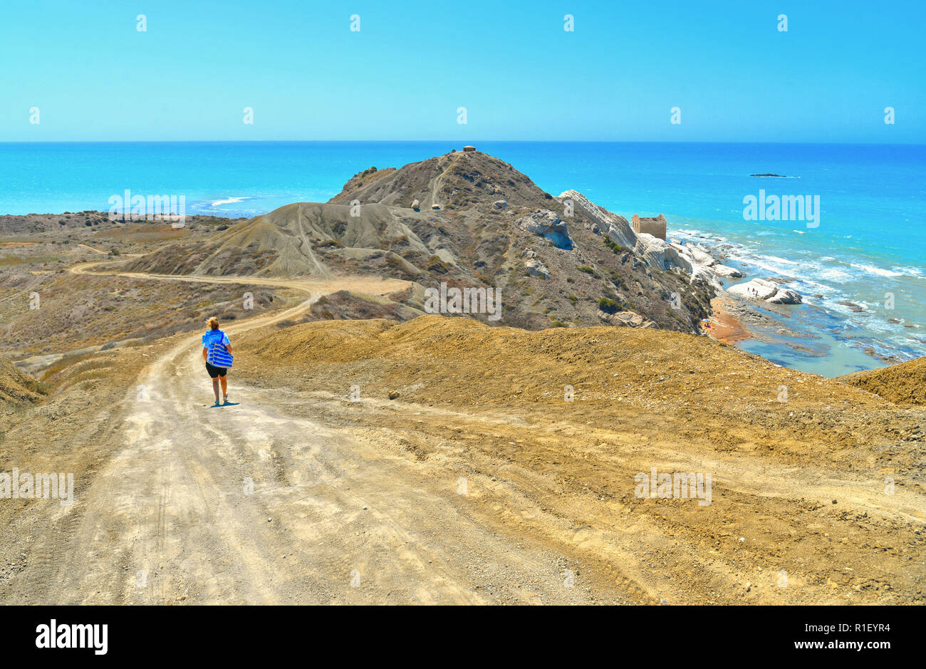 Giovane donna cammina su un deserto di strada sterrata su un promontorio verso il mare e la spiaggia solitaria in giorno di estate Foto Stock