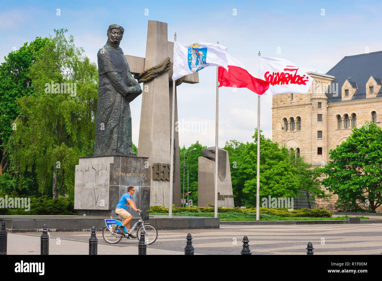 Poznan monumento, un ciclista cavalca la sua moto passato il Monumento alle Vittime del giugno 1956 in piazza Adam Mickiewicz (Plac Mickiewicza), Poznan, Polonia. Foto Stock