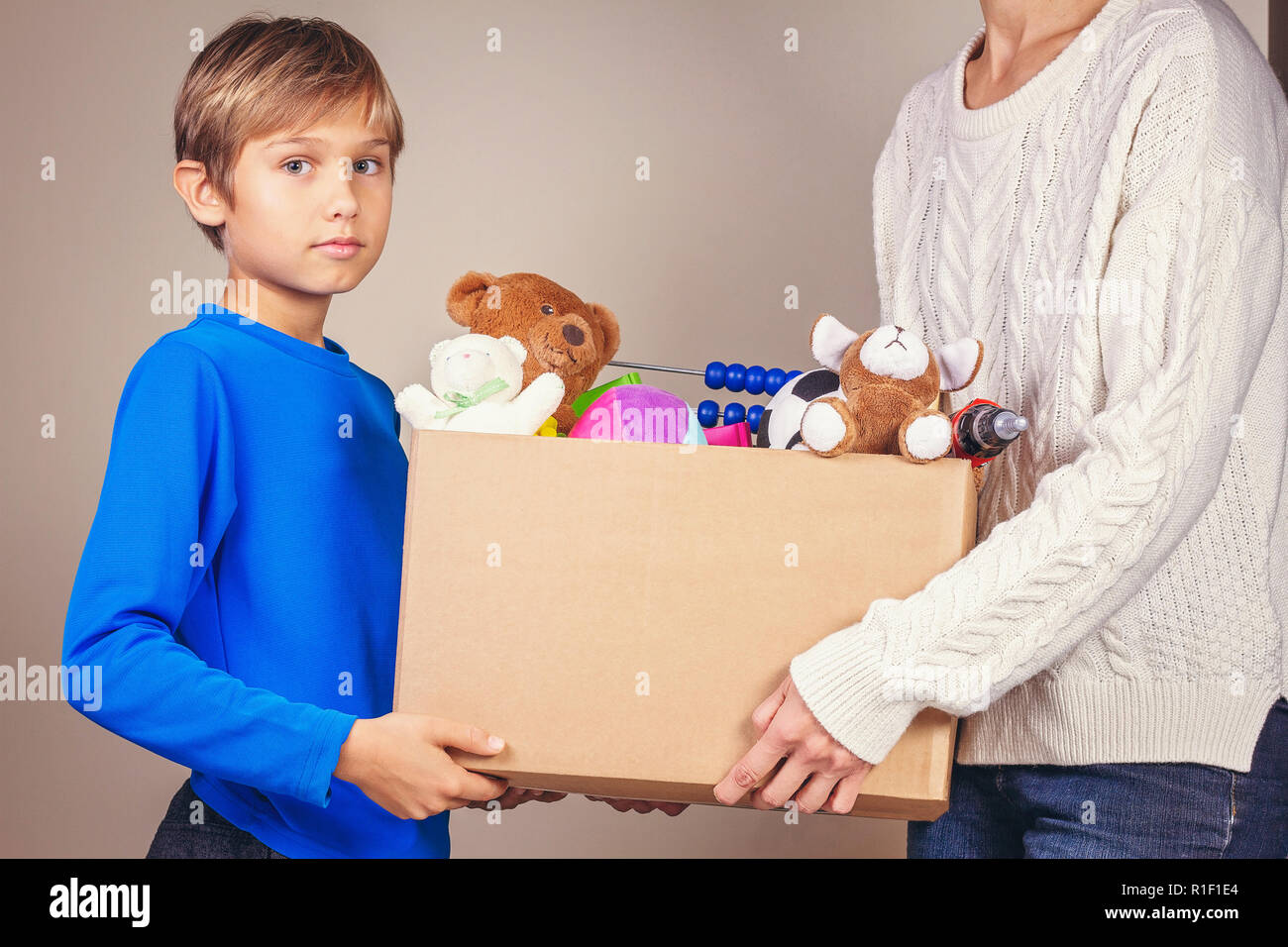 Concetto di donazione. Donare il box con abiti, libri e giocattoli nei membri della famiglia mano Foto Stock