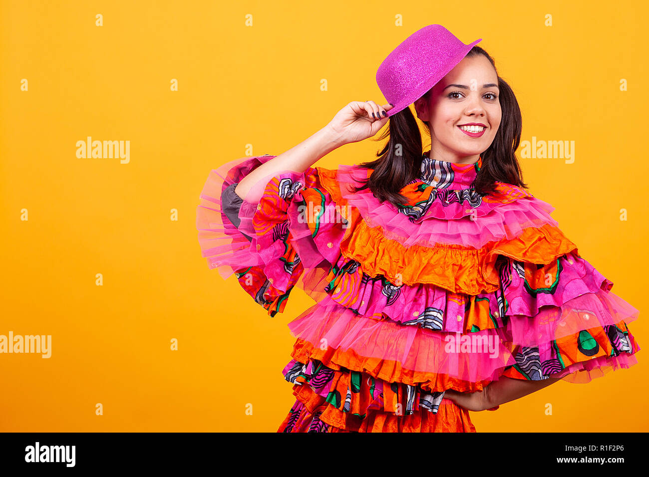 Giovane bella donna che indossa un mascarade costume latino su sfondo giallo in studio Foto Stock