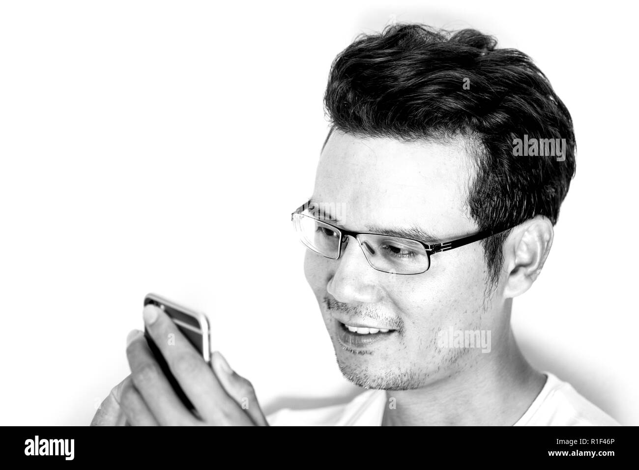 Bel uomo asiatico con leggera barba e capelli ricci indossare occhiali per vicino avvistato utilizza lo smartphone. Il sorriso e felice. Effetto monotona. Foto Stock